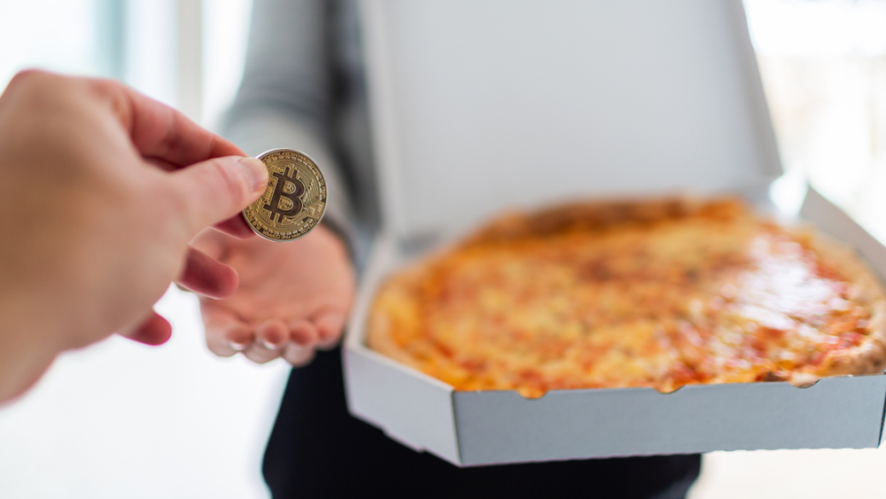 Osoba plaća picu Bitcoin novčićem tokom simbolične kupovine hrane kriptovalutom.